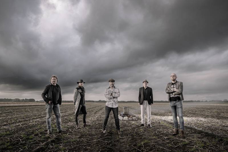 The Sidekicks bandfoto - bandleden op het Groninger land tegen een typisch Groningse lucht met wolken met op de achtergrond een grafmonumentje