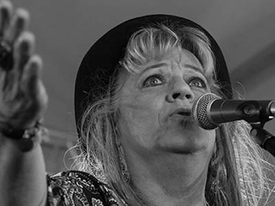 Gina's band of Blues promofoto - zangeres Gina de Boer met een hoed zingend in een Shure SM58 microfoon
